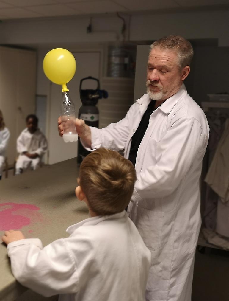 man i vit labrock utför experiment med ballong framför barn