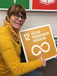 Therese Rahm i gul tröja håller upp en gul skylt där det står 12 Hållbar konsumtion och produktion. Ett av de globala hållbarhetsmålen.